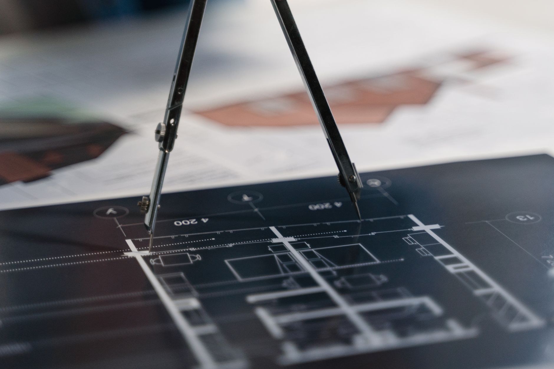 Close-up of a compass on architectural blueprints with various designs in the background.